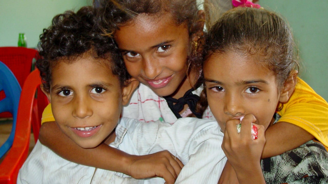 Three young children pose together and smile at the camera