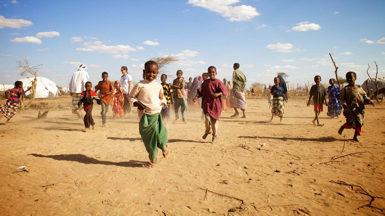 Group of child refugees in Dadaab camp, running around on a dirt field