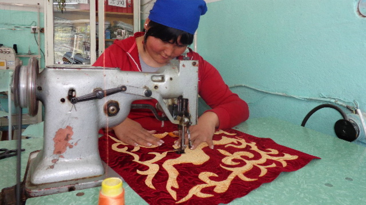 Woman using a sewing machine on a piece of red fabric with gold decor.