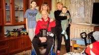 Oleksandr with his wife Victoria and their three children, Mikhail, Natalia and little Alexander, in their flat in Mykolaiv. Since he was seriously injured in an air strike in 2022, his family has played an essential role in his care.  A man is sitting in a wheelchair in an apartment surrounded by his family.