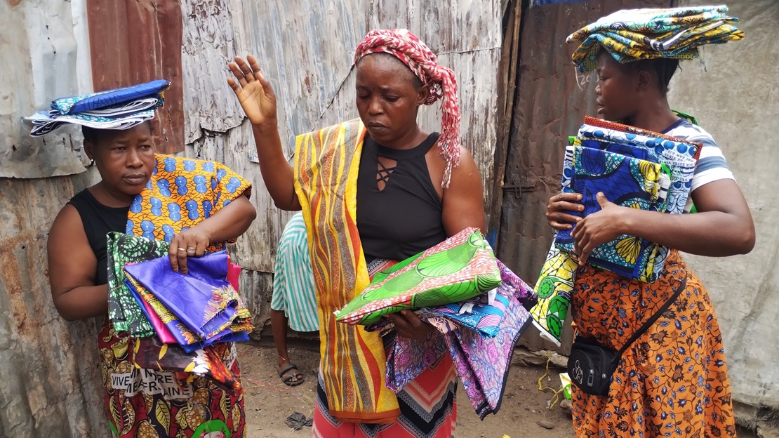 Three women are at the center of the image, each carrying fabric to be used in their trade.